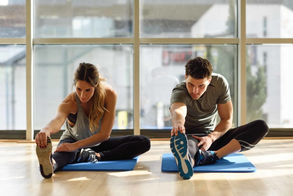 Two people streching their legs in gym.