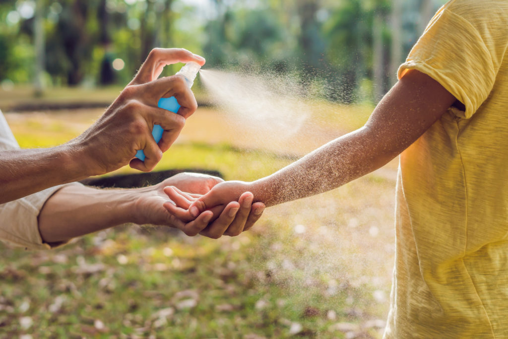 Dad and son use Sunscreen spray on skin outdoors.